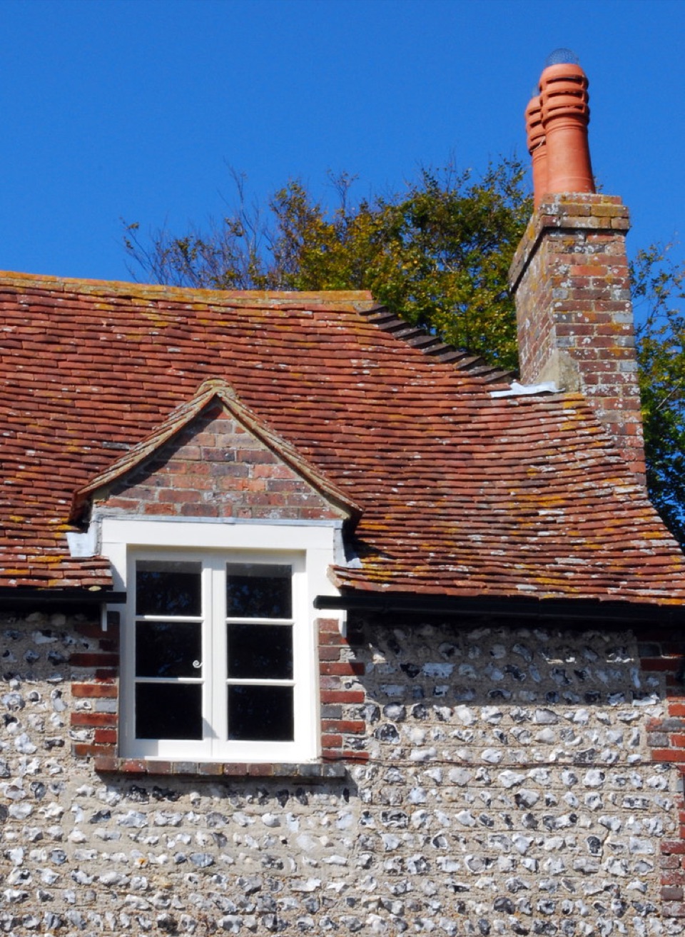A flint wall with brick dressings under a tiled roof and a dormer at East Dean in East Sussex